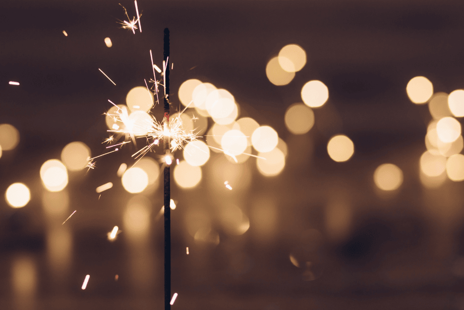 A single sparkler burning in front of a blurred background of lights on a dark night