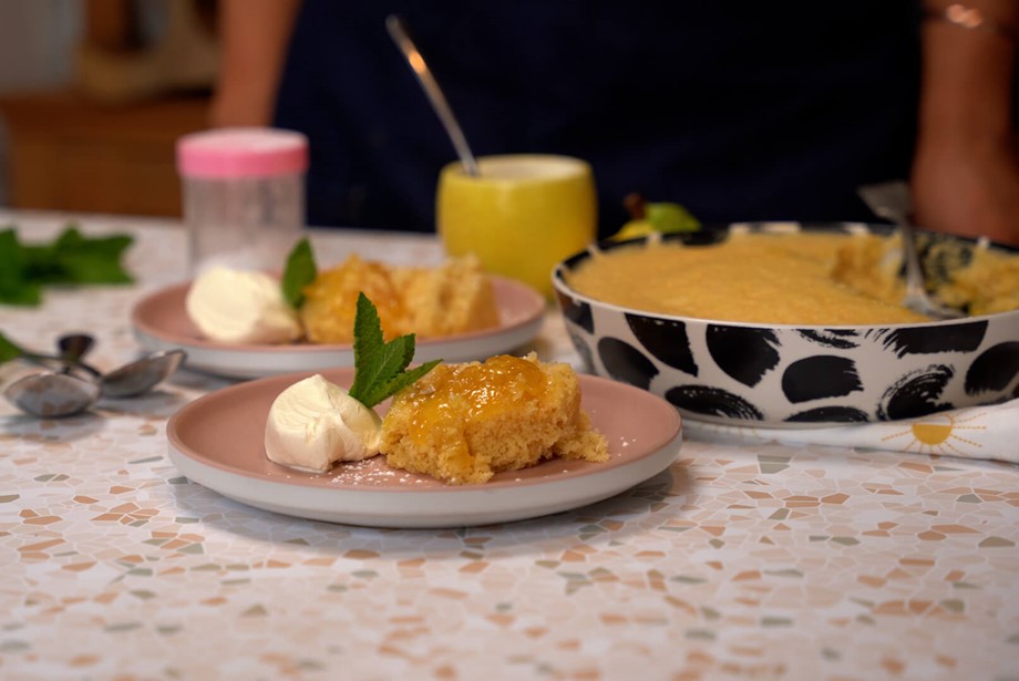 Spoonful of fluffy sponge luscious lemon pudding and creme fraiche on a pink plate with more servings in the background