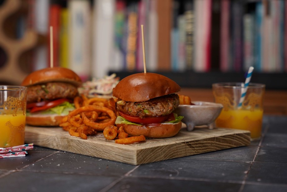 A wooden board with teriyaki pork burgers in buns with curly fries and drinks