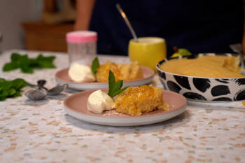 Spoonful of fluffy sponge luscious lemon pudding and creme fraiche on a pink plate with more servings in the background