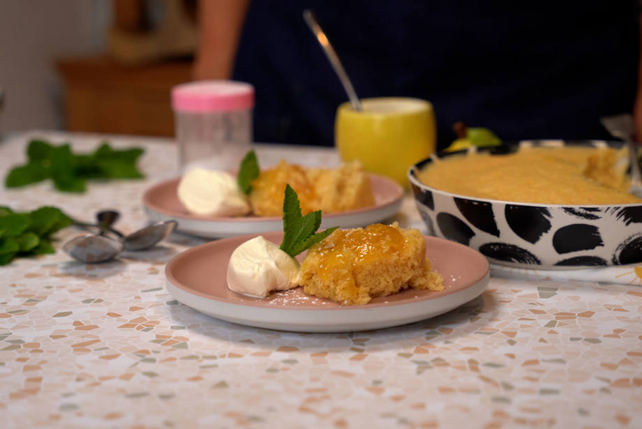 Spoonful of fluffy sponge luscious lemon pudding and creme fraiche on a pink plate with more servings in the background