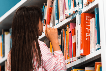 Photo of a dark haired girl selecting a book in a library. Photo by Rabie Madaci on Unsplash