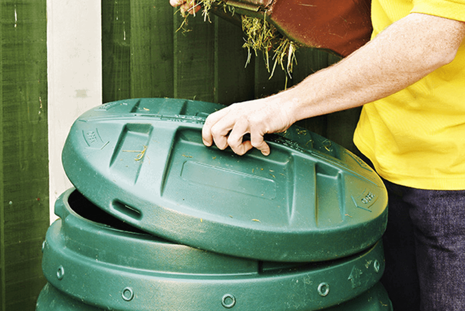 Adding garden waste into a plastic compost bin